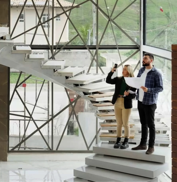 casal de arquitetos parados na escada segurando smartphone e papéis